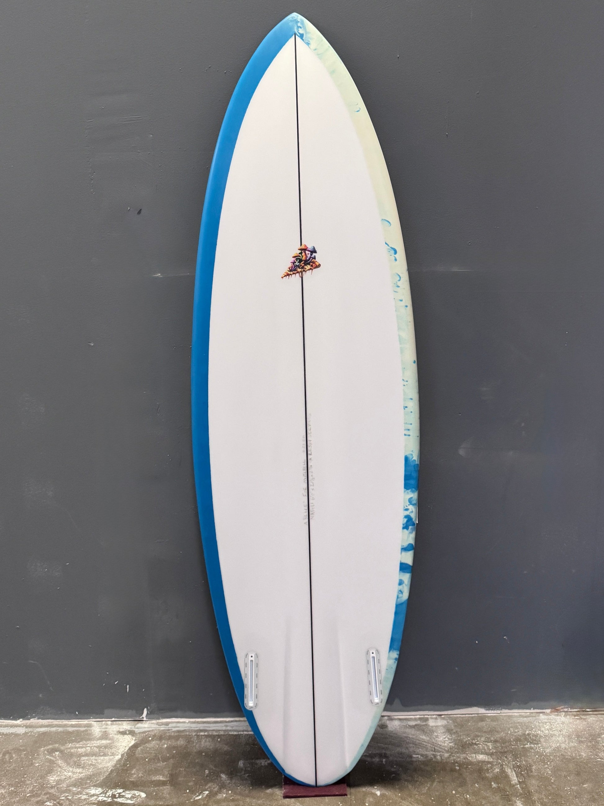 Surfboard with blue and white design leaning against a dark wall.